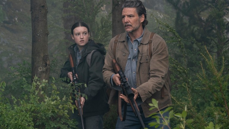 Joel (Pedro Pascal) and Ellie (Bella Ramsey) stand on alert in a forest in The Last of Us season 2
